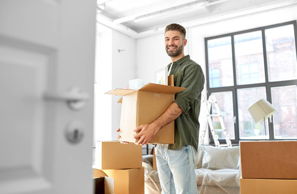 moving, people and real estate concept - happy smiling man holding box with stuff at new home - Photo, Image