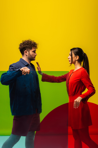 brunette woman showing stop to curly man and holding different shapes glass isolated on yellow - Foto, Imagem