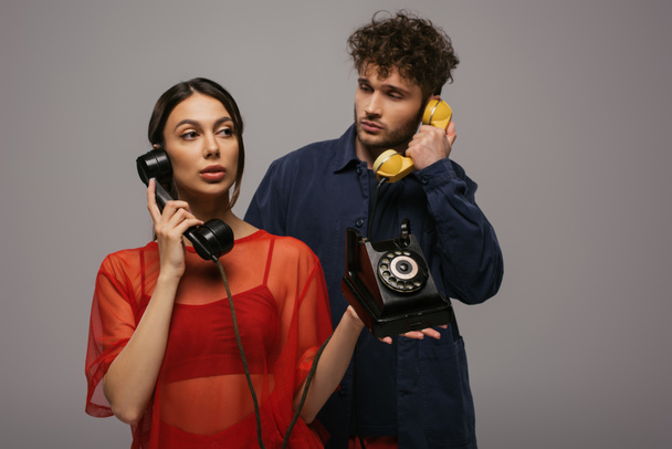 young woman and curly man holding retro handsets while having phone call isolated on grey - Foto, imagen