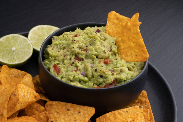 Guacamole dip with tortilla chips or nachos and lime on a black background. High quality photo - Valokuva, kuva