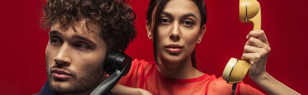 young woman and curly man holding retro handsets while posing on red, banner - Foto, Imagen
