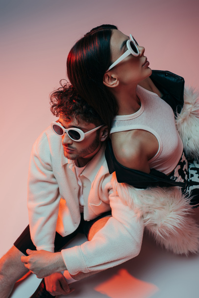 high angle view of stylish man in sunglasses and woman in faux fur jacket sitting on pink and grey - Valokuva, kuva