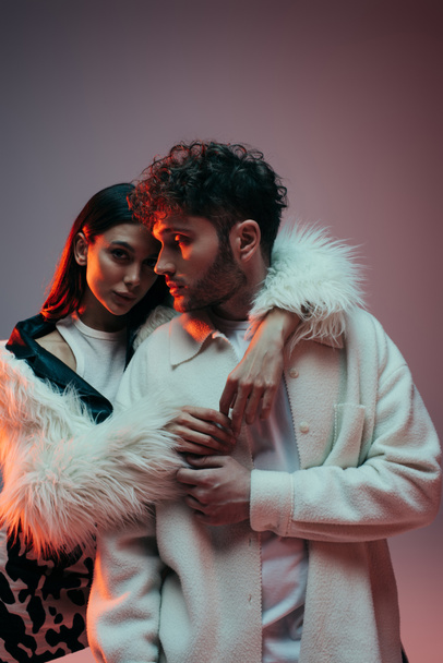 stylish young woman in faux fur jacket hugging curly man on grey - Foto, immagini