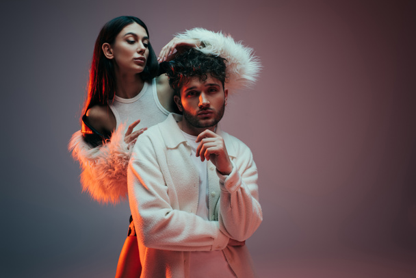 young woman in faux fur jacket gesturing near pensive man posing on grey - Photo, image