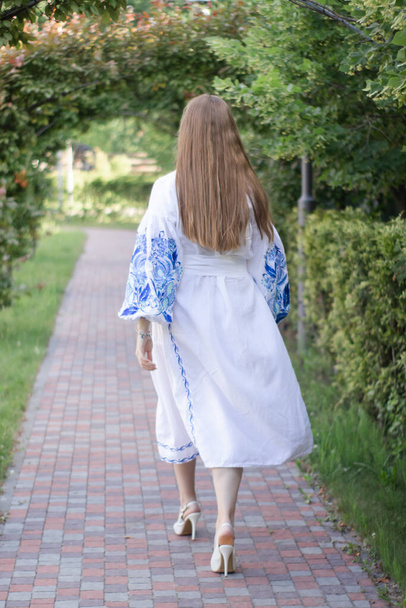 Portrait of young Ukrainian woman dressed in blue national traditional embroidered shirt in park outdoor. - Fotó, kép