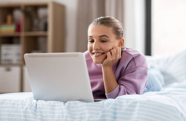 children, technology and internet concept - happy smiling student girl with laptop computer at home - Foto, Bild