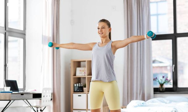fitness, sport and healthy lifestyle concept - happy teenage girl with dumbbells exercising at home - Fotó, kép