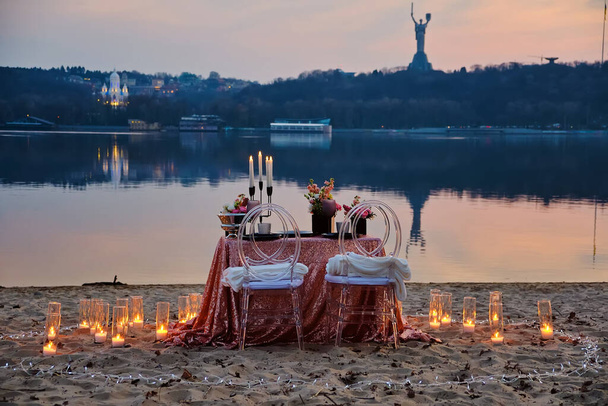 A date on the river bank, a decorated table is waiting for a couple in love. City lights in the background, evening Kyiv, Ukraine. - Valokuva, kuva