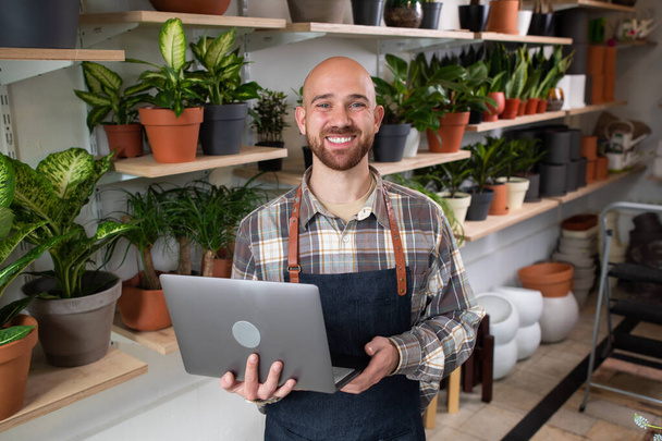 Handsome Caucasian man holding his laptop while working on his own floral shop in front of the camera he smiling large happy concept of entrepreneur and small business. Portrait - Foto, imagen