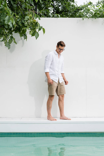 full length of barefoot man in shirt standing over pool near white wall - 写真・画像