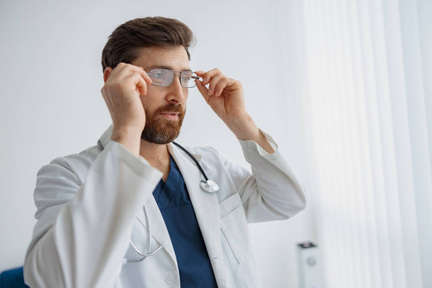 Doctor wearing glasses standing in medicine clinic hall and looking away. High quality photo - Фото, изображение