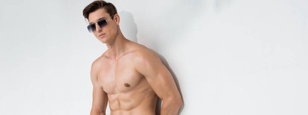 man with athletic body posing in sunglasses on white background, banner - Photo, Image