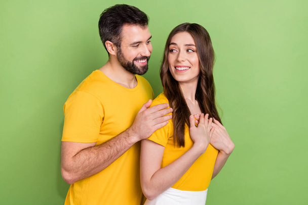 Profile portrait of cheerful two partners hug hands touch shoulders look each other isolated on green color background. - Фото, изображение