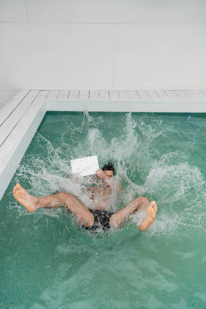 high angle view of man with laptop falling in pool with water splashes - Fotó, kép
