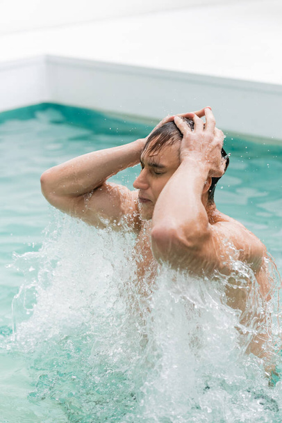 чоловік із закритими очима торкається мокрого волосся під час купання в басейні
 - Фото, зображення
