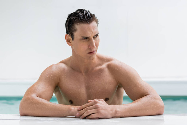 wet and pensive man with muscular body looking away at poolside - Foto, immagini