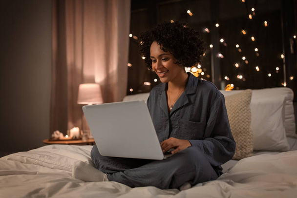 technology, bedtime and rest concept - happy smiling woman in pajamas with laptop computer sitting in bed at night - Foto, Bild