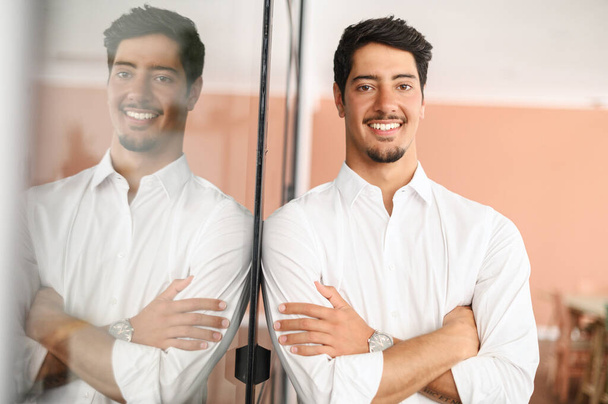 Smiling hispanic male employee wearing smart casual shirt stands with arms crossed in modern coworking space, cheerful proud latin businessman looks at camera posing indoors - Photo, Image