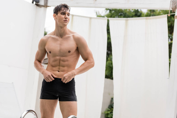 wet sportive man in swimming trunks looking away outdoors - Photo, image