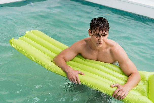 wet man swimming with inflatable mattress in pool with turquoise water - Photo, Image