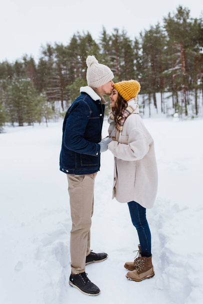 people, love and leisure concept - happy man kissing woman to forehead in winter forest - Foto, imagen