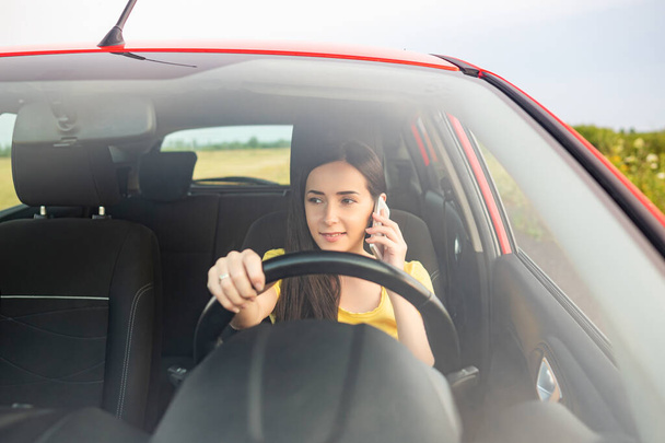 Молодая женщина использует смартфон во время вождения автомобиля. - Фото, изображение