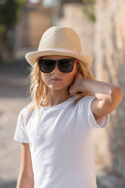 Portrait of a child in a white t-shirt, hat and sunglasses in sunny weather. - Valokuva, kuva