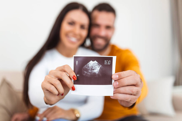 Woman and her boyfriend holding up an image of her sonogram of the baby. Young happy Couple with baby ultrasound photo - Φωτογραφία, εικόνα