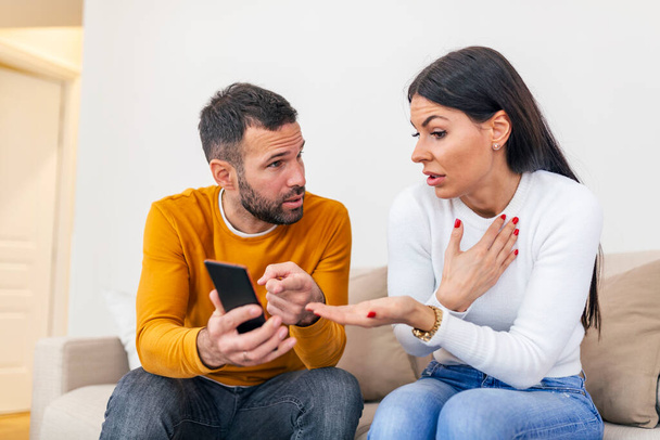 Angry couple or marriage fighting for a mobile phone at home. Jealous caucasian man holding smart phone and showing message to his wife - Foto, Bild
