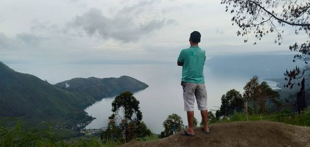 A lonely man contemplating while enjoy Lake Toba in the evening. Lake Toba is one of great destination in Indonesia - Φωτογραφία, εικόνα