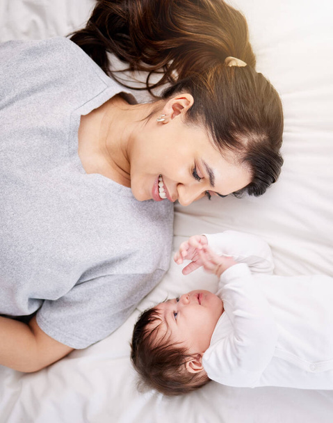 Egyetlen kevert fajú spanyol nő kötődik az újszülött gyerekéhez, miközben az ágyban beszél és jól érzi magát. Spanyol nő élvezi, hogy anya, miközben mosolyog, és beszél az ő aranyos kis baba. - Fotó, kép