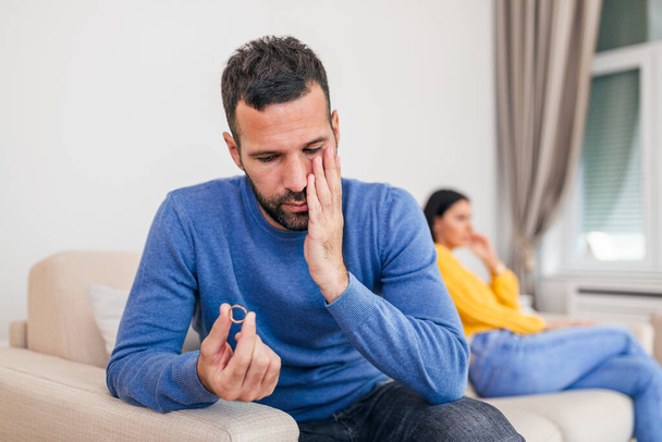 Stressed man holding her wedding ring worried about breakup or divorce, avoid talking with wife after fight, anxious couple ignore each other. Frustrated sad husband taking off the wedding ring - Foto, Imagem