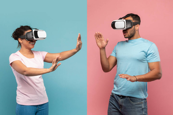 Young black spouses in VR headset touching air during virtual reality experience, man and woman exploring artificial computer world or playing video game, blue and pink studio background - Photo, image