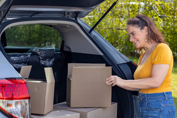 Caucasian mature woman is holding cardboard box to packing inside the car for house moving and relocation - Photo, image