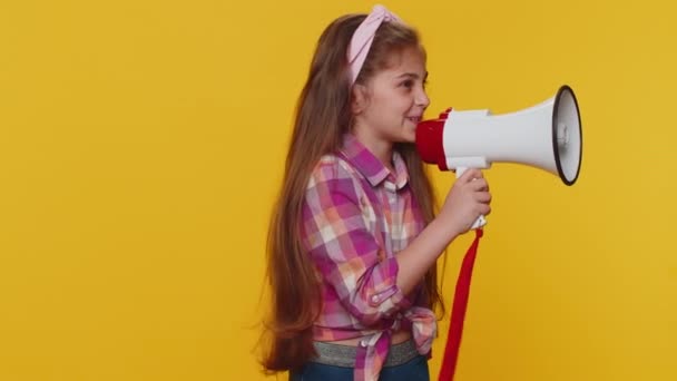 Preteen child girl kid talking with megaphone, proclaiming news, loudly announcing advertisement warning using loudspeaker to shout speech. Little toddler children isolated on studio yellow background - Metraje, vídeo