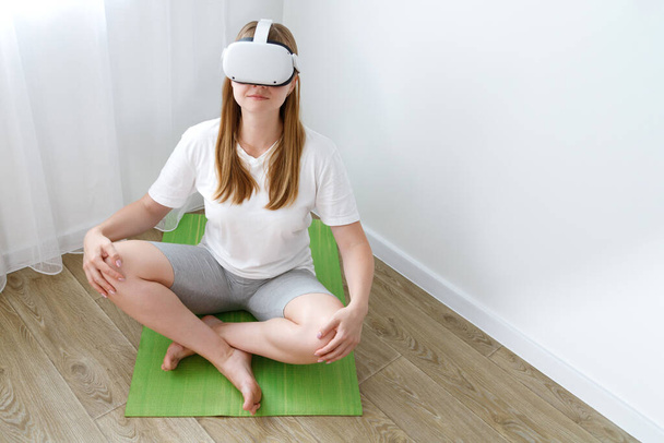 een vrouw in VR Oculus op een sportmat doet yoga - Foto, afbeelding