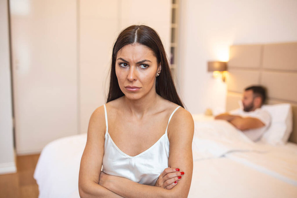 Couple ignoring each other in bed, Unhappy young heterosexual couple in bedroom. Sad Woman Sitting At The Edge Of Bed In Front Of Man - Fotografie, Obrázek