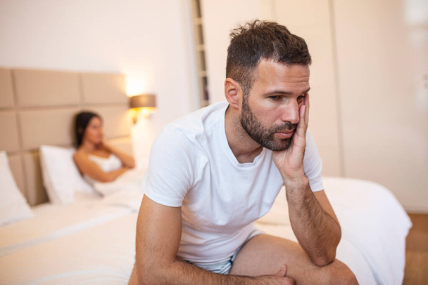 Beautiful girl and a frustrated man sitting in bed and not looking at each other. Upset couple ignoring each other. Worried man in tension at bed. Young couple angry with each other after a fight. - Photo, Image