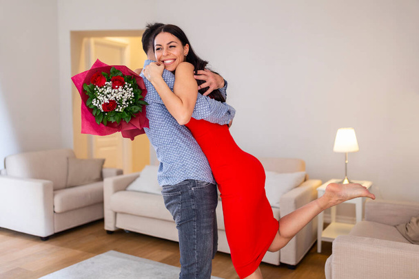 Beautiful young couple at home. Hugging, kissing and enjoying spending time together while celebrating Saint Valentine's Day with red roses - Фото, зображення