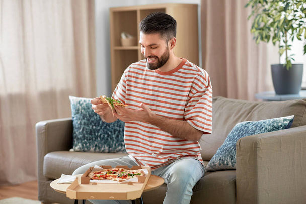 jídlo dodávky, spotřeba a lidé koncept - šťastný muž jíst donášku pizzy doma - Fotografie, Obrázek