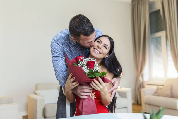 Affectionate young man giving his beautiful young wife a bouquet of red roses and kissing her on Valentines day , romantic happy couples sharing gift together on Valentines day - Fotoğraf, Görsel