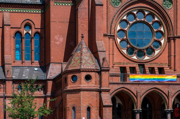 Detail shot of the entrance area and the facade of the Heilig-Kreuz-Church in Berlin Kreuzberg. A rainbow flag hangs over the entrance. - Valokuva, kuva