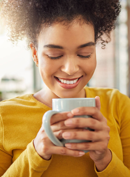 Young cheerful mixed race woman holding and drinking a cup of coffee at home. One comfy hispanic female enjoying a cup of tea while relaxing at home. - Φωτογραφία, εικόνα