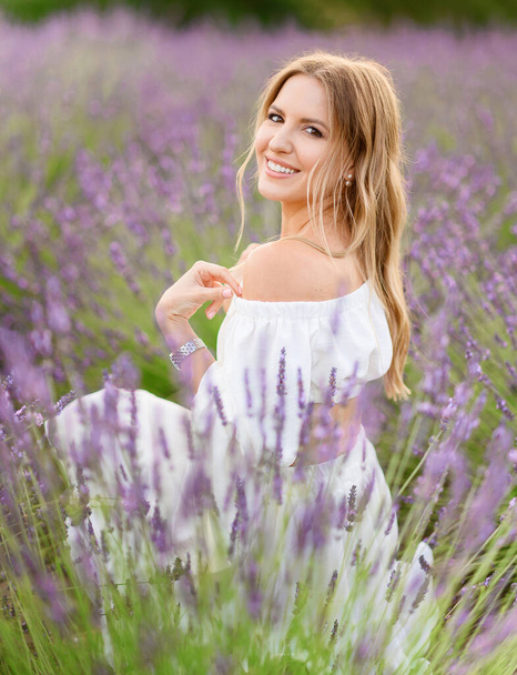 Portrait of a beautiful young girl in a white summer dress in a lavender field at sunset - Foto, Bild