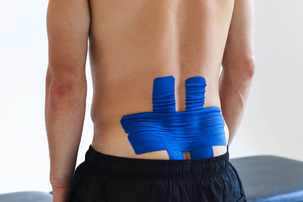 Physical therapist applying kinesio tape on male patient's lower back. Kinesiology, physical therapy, rehabilitation concept. - 写真・画像
