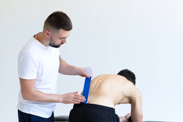 Physiotherapeut legt Kinesiotape auf den unteren Rücken des männlichen Patienten. Kinesiologie, Physiotherapie, Rehabilitationskonzept. - Foto, Bild