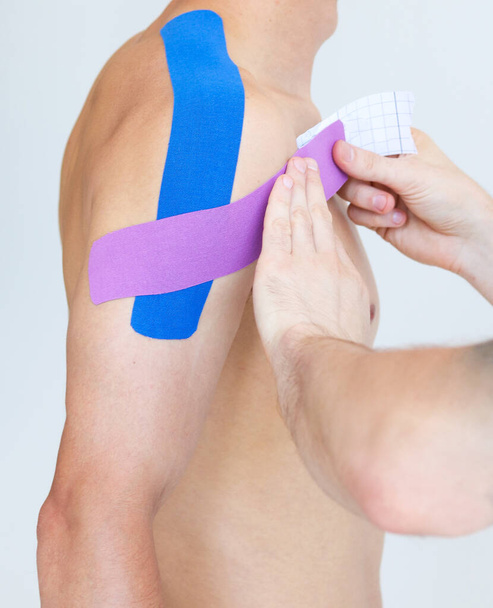Kinesiology taping. Physical therapist applying kinesiology tape to patient shoulder. Male therapist treating injured shoulder of male athlete. Post traumatic rehabilitation, sport physical therapy. - Photo, image