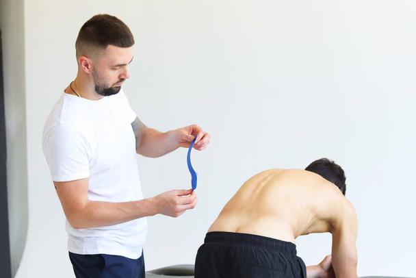 Physical therapist applying kinesio tape on male patient's lower back. Kinesiology, physical therapy, rehabilitation concept. - Фото, изображение