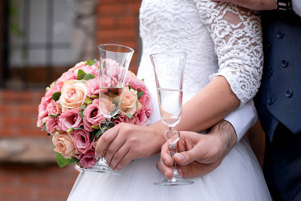 wedding bouquet in the hands of the bride and groom at the ceremony. glasses of champagne. floristry for the holiday. idea for wedding event agencie - Fotó, kép