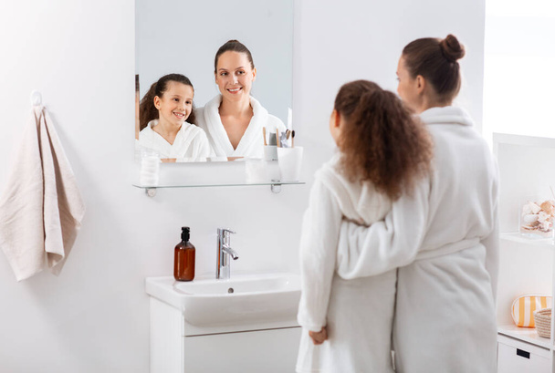 beauty, hygiene, morning and people concept - happy smiling mother and daughter looking to mirror at bathroom - Фото, зображення